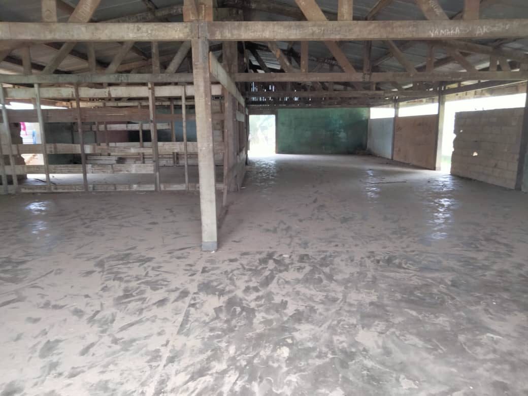 Intérieur vide du bâtiment : charpente en bois apparente, sol en terre poussiéreux